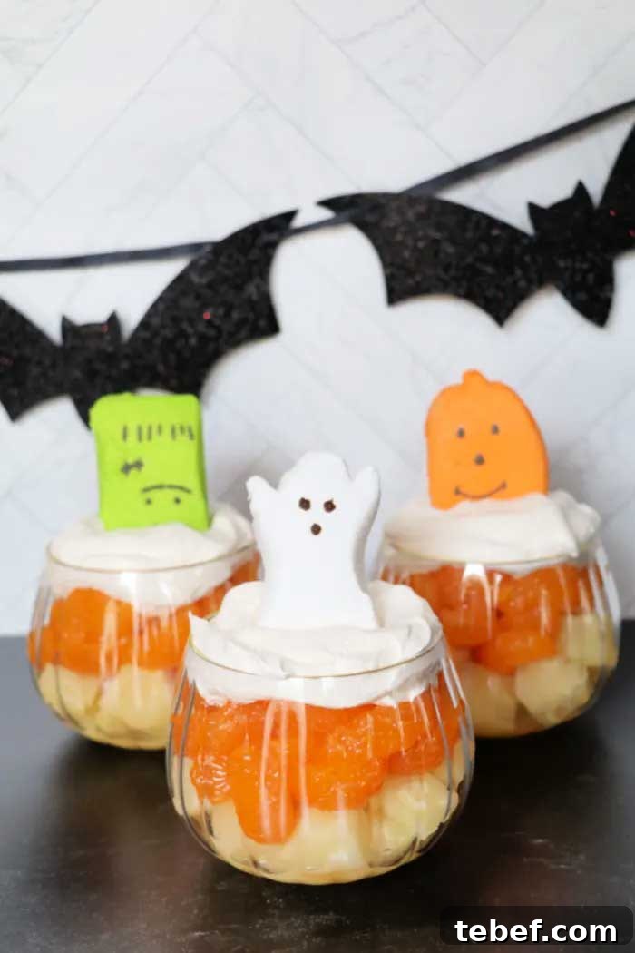 3 Halloween fruit cups - one decorated with a ghost, one a jack-o'-lantern, and one a Frankenstein; with decorative bats in background.