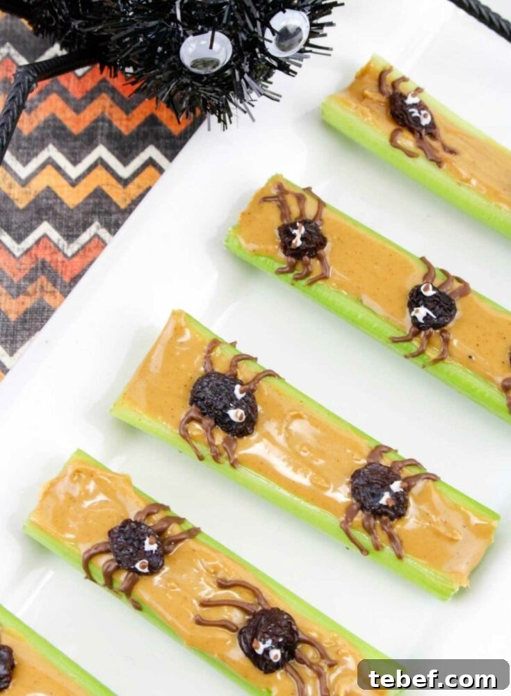 Several finished celery sticks lined up on white plate with spider decoration peering at them.