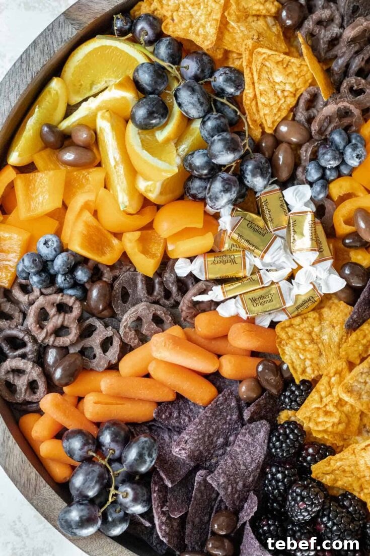 Overhead of left side of snack board with Halloween-colored fruit, chips and candy.