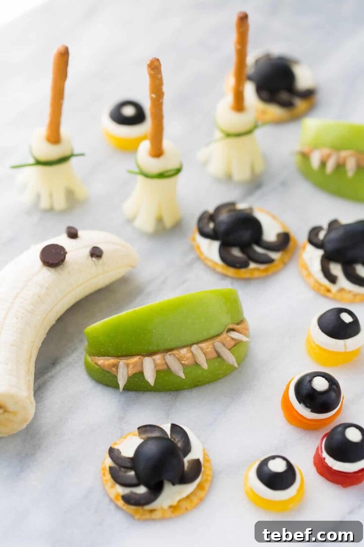 Variety of gluten free Halloween snacks on white marble surface, including a banana ghost, apple teeth, and olive spiders and eyeballs.