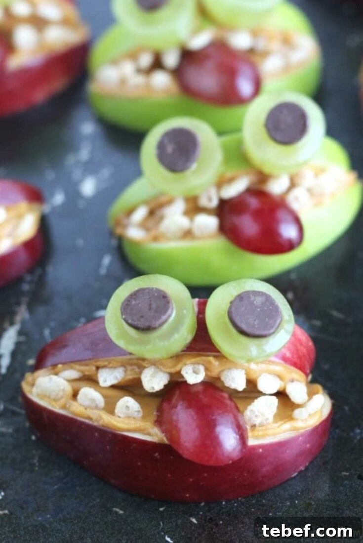 Monster made of red apple in front, with others made of green apple behind it on black surface.