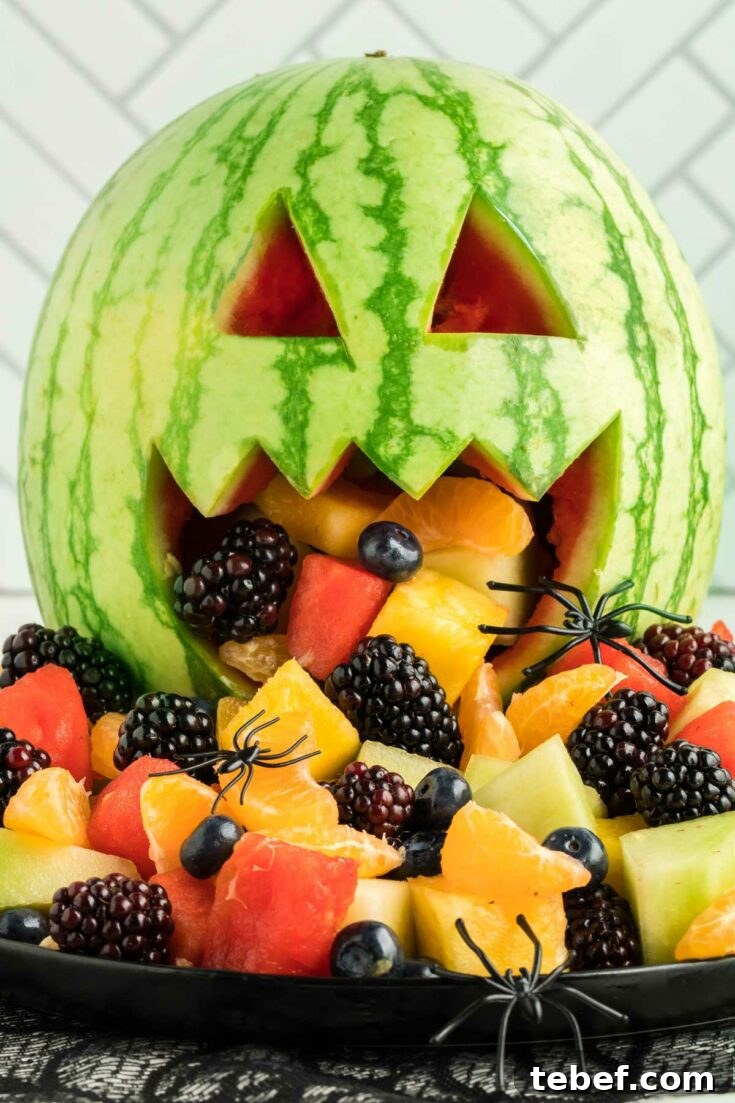 Carved Watermelon barfing fresh fruit onto black serving tray, with plastic Halloween spiders decorating it.