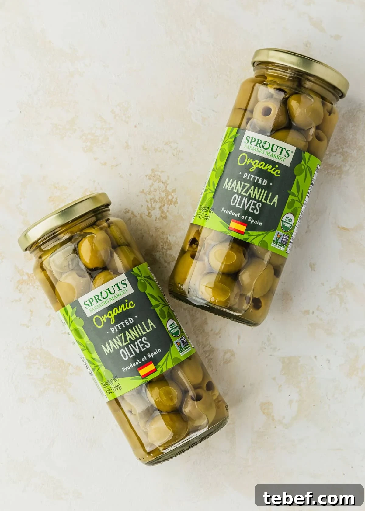 Citrus-Marinated Spanish Olives with Manchego Cheese 3 Jars of Manzanilla olives on a beige counter.