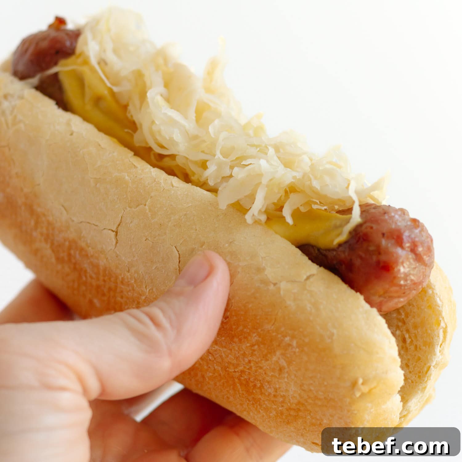 Grilled Bratwurst: Two Proven Methods for Perfect Brats 9 Hand holding bratwurst on a bun topped with mustard and sauerkraut.