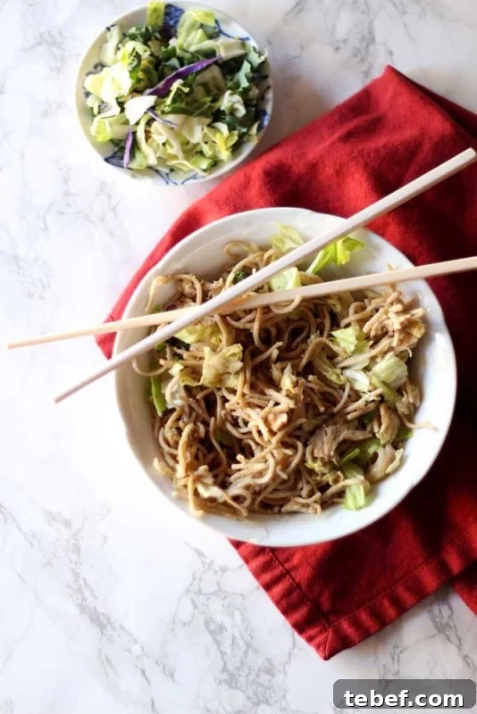 White bowl containing Thai Peanut Chicken Pasta, sitting on red napkin with cross chopsticks.