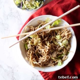 White bowl containing Thai Peanut Chicken Pasta, sitting on red napkin with cross chopsticks.