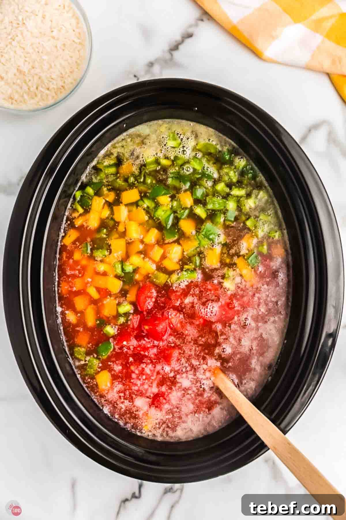 Slow Cooker Stuffed Pepper Soup Recipe for Comforting Weeknights 6 crock pot with bell peppers and tomatoes being stirred with a wood spoon