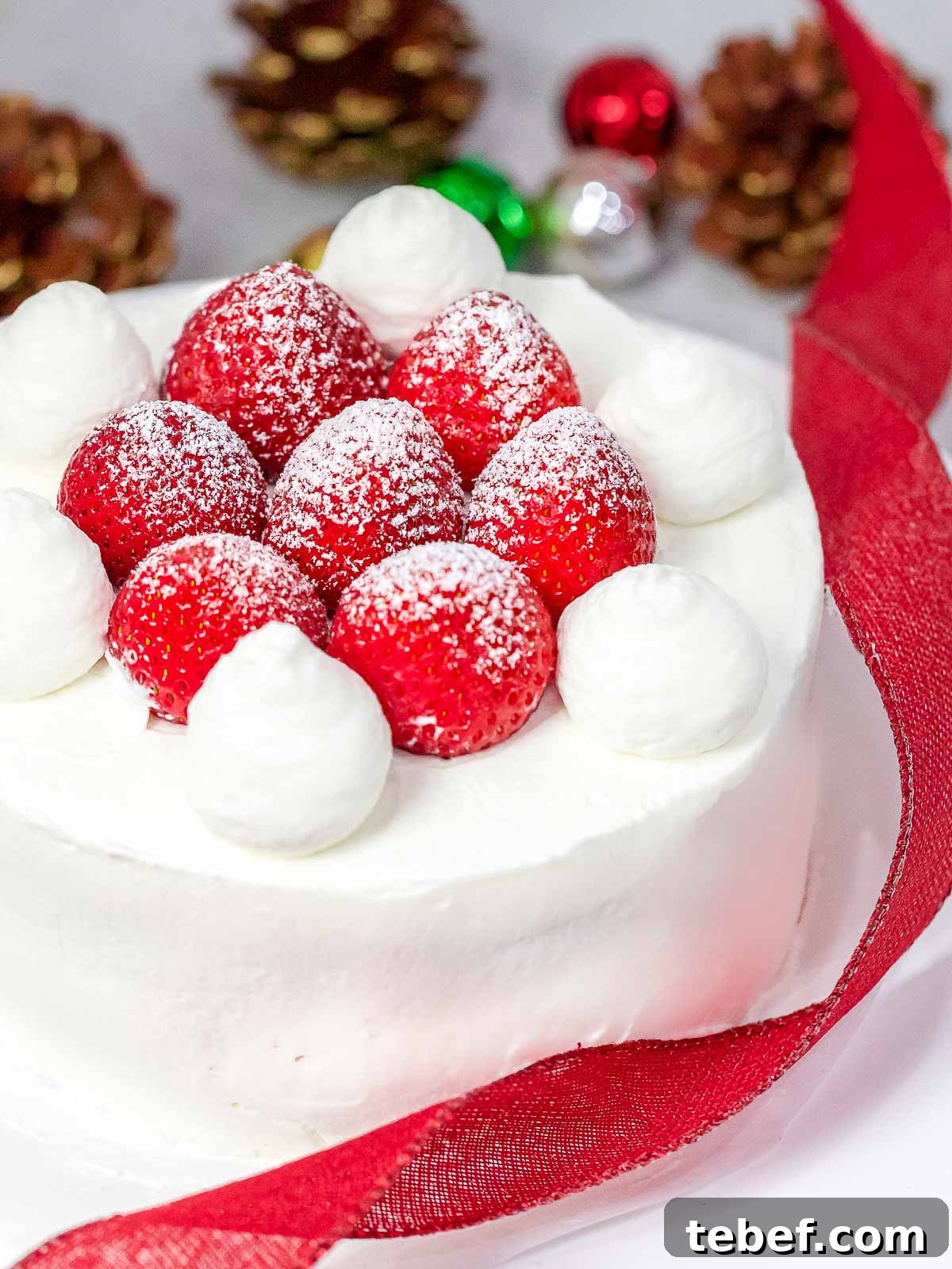 Authentic Japanese Strawberry Shortcake Recipe — Light, Fluffy Layers 11 Japanese Christmas cake decorated with fresh strawberries and whipped cream next to red ribbon, Christmas ornaments, and pine cones in the background