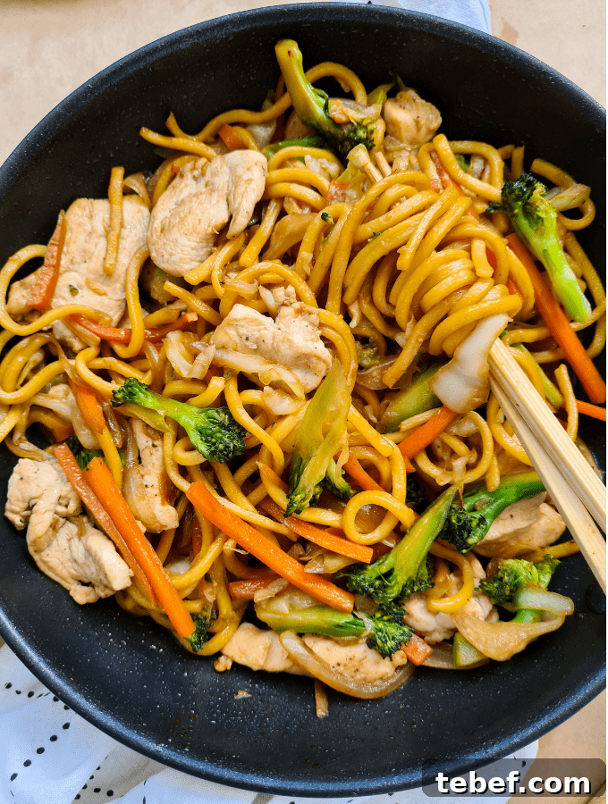 Chicken Noodle Stir-Fry with Garlic Soy Glaze 11 A pair of chopsticks twirling up hokkien noodles in a pan full of cooked noodles, chicken and vegetables