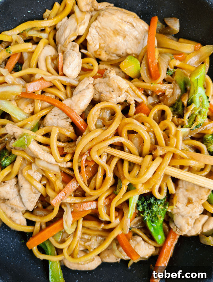 Chicken Noodle Stir-Fry with Garlic Soy Glaze 10 Close up of noodles, chicken breasts and broccoli in a frying pan. A pair of chopsticks picking up noodles
