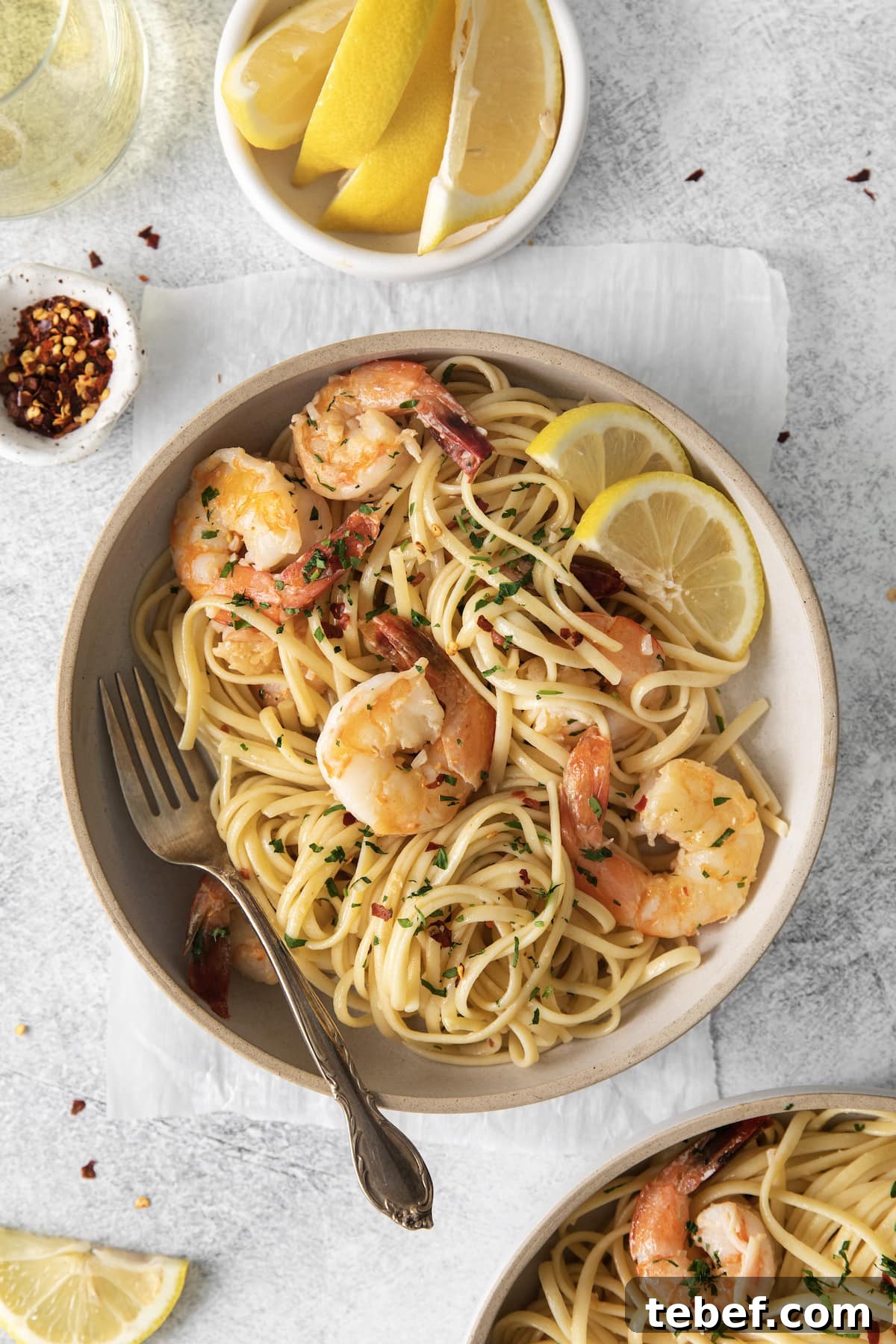 Garlic Butter Shrimp Scampi Recipe for Quick Weeknight Meals 15 shrimp pasta with linguine, red pepper flakes, herbs, and lemon slices in a bowl