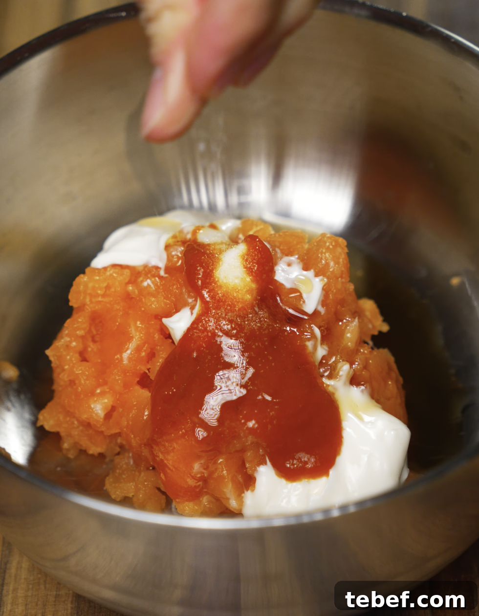 A metal bowl filled with chopped salmon, mayonnaise, and sriracha being seasoned with salt. This spicy creamy mixture will be used as a topping for crispy rice bites.