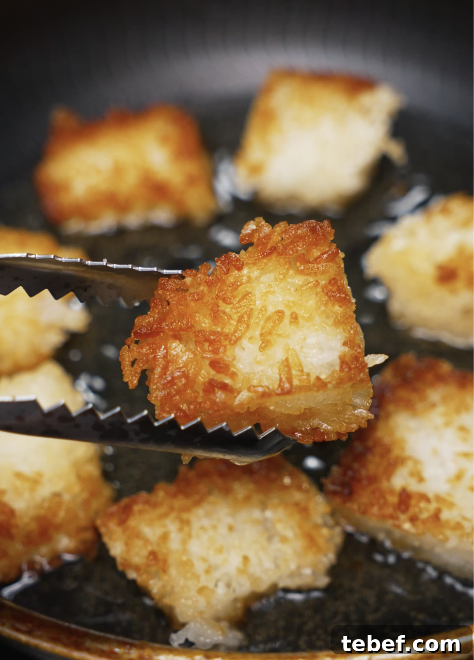 Golden brown rice cubes frying in oil with a close-up view of a crispy piece held by tongs. The exterior is perfectly crisp, making it the ideal base for spicy salmon toppings.