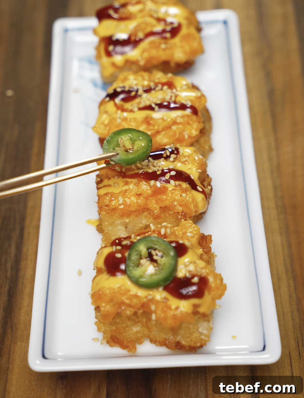 Chopsticks placing a slice of fresh jalapeño onto a golden, crispy salmon rice bite drizzled with spicy mayo and soy glaze, garnished with sesame seeds on a white platter.