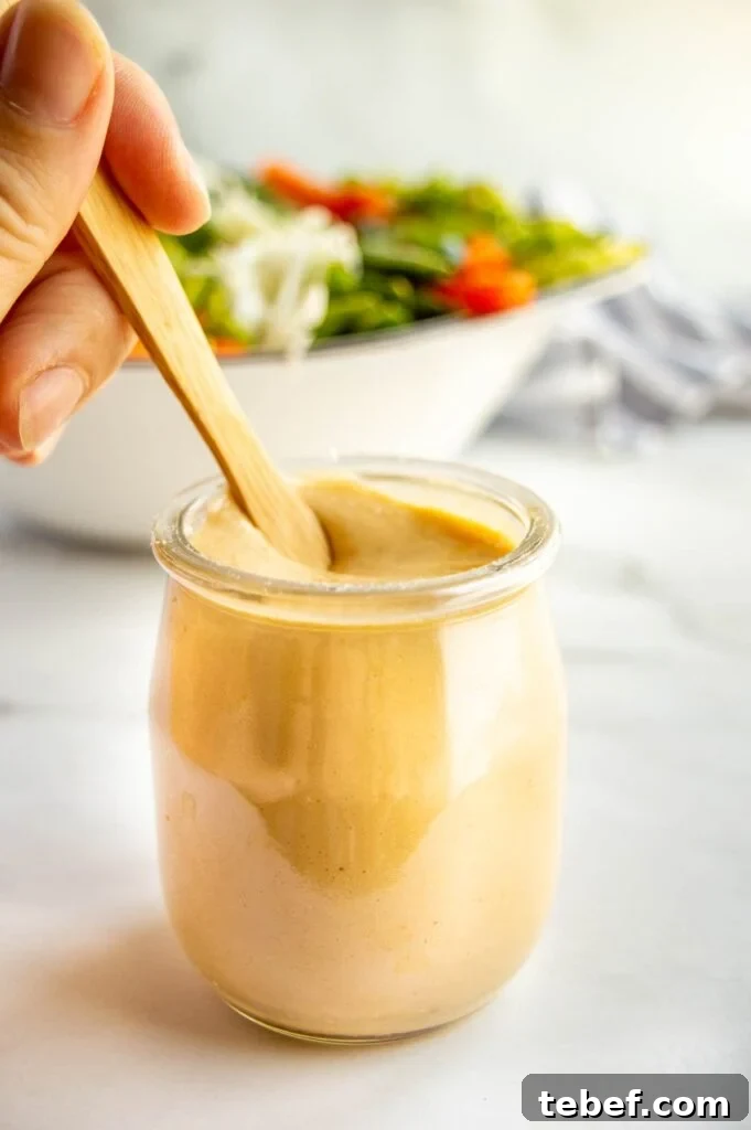 A glass jar with thick light brown dressing in it being stirred by a hand