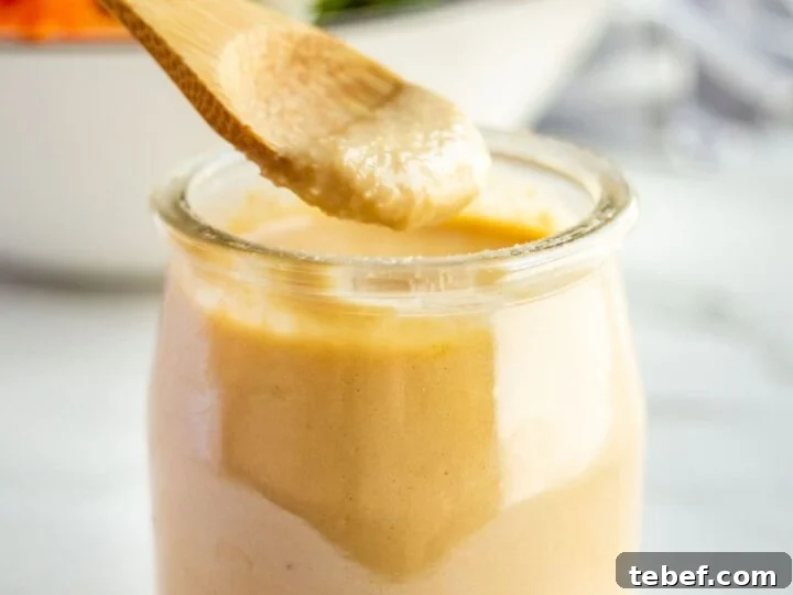A wooden spoon dipping into a small glass jar of creamy light brown dressing.
