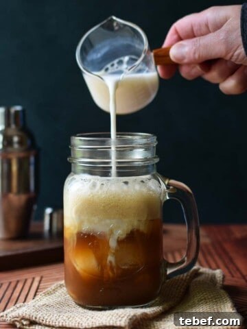 Milk being poured into a clear mug with chai tea.