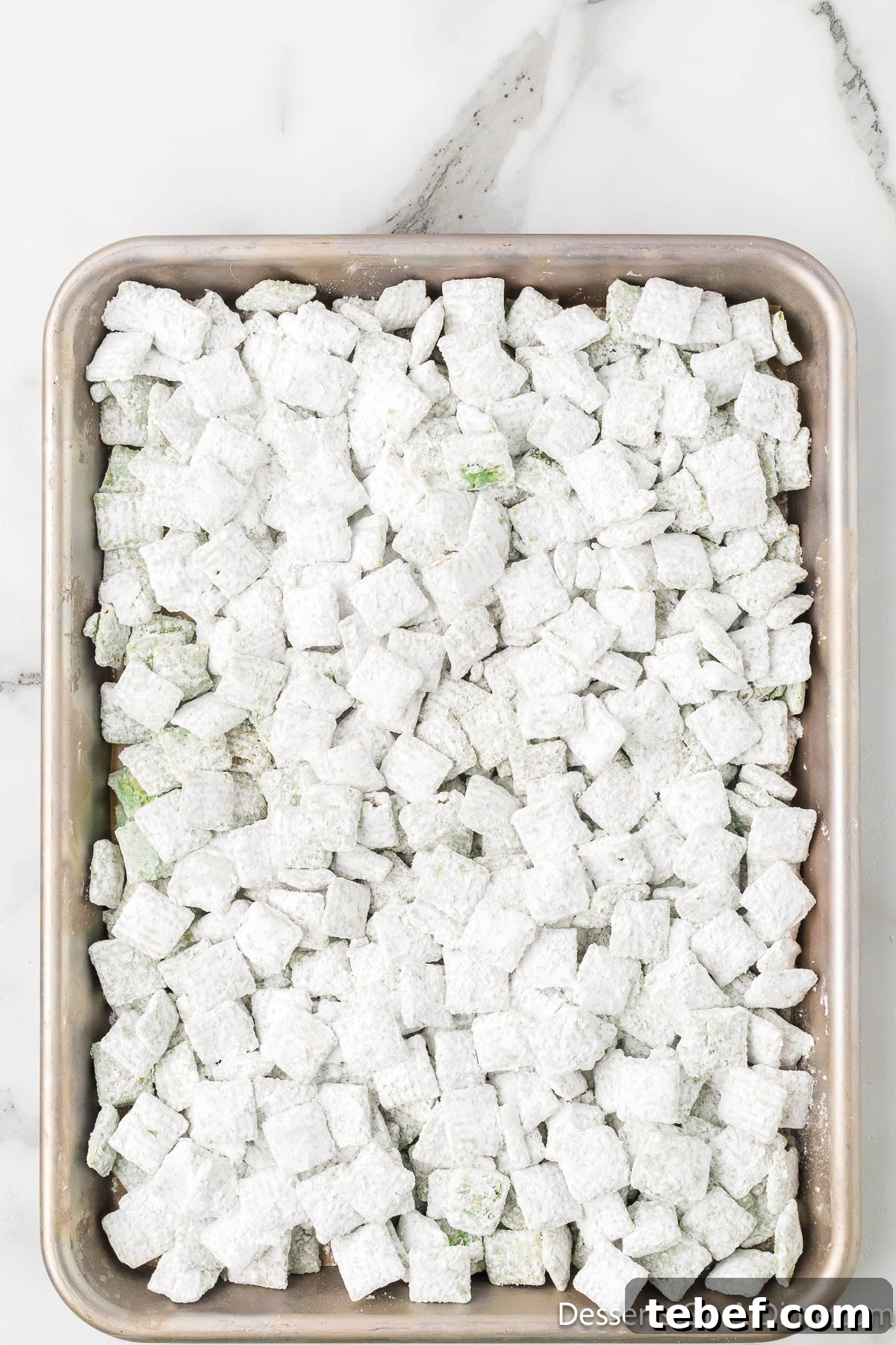Grinch Puppy Chow Holiday Snack Mix Recipe 8 Cereal coated in powdered sugar and spread on baking sheet.