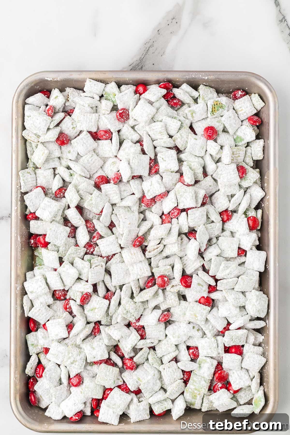 Grinch Puppy Chow Holiday Snack Mix Recipe 9 Red M&M's added to mixture on baking sheet.