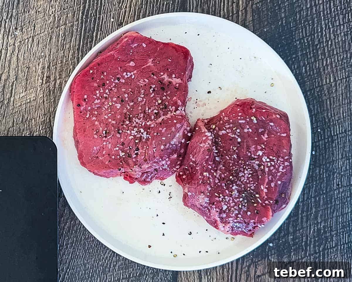 Oiled and seasoned steaks on a white plate.
