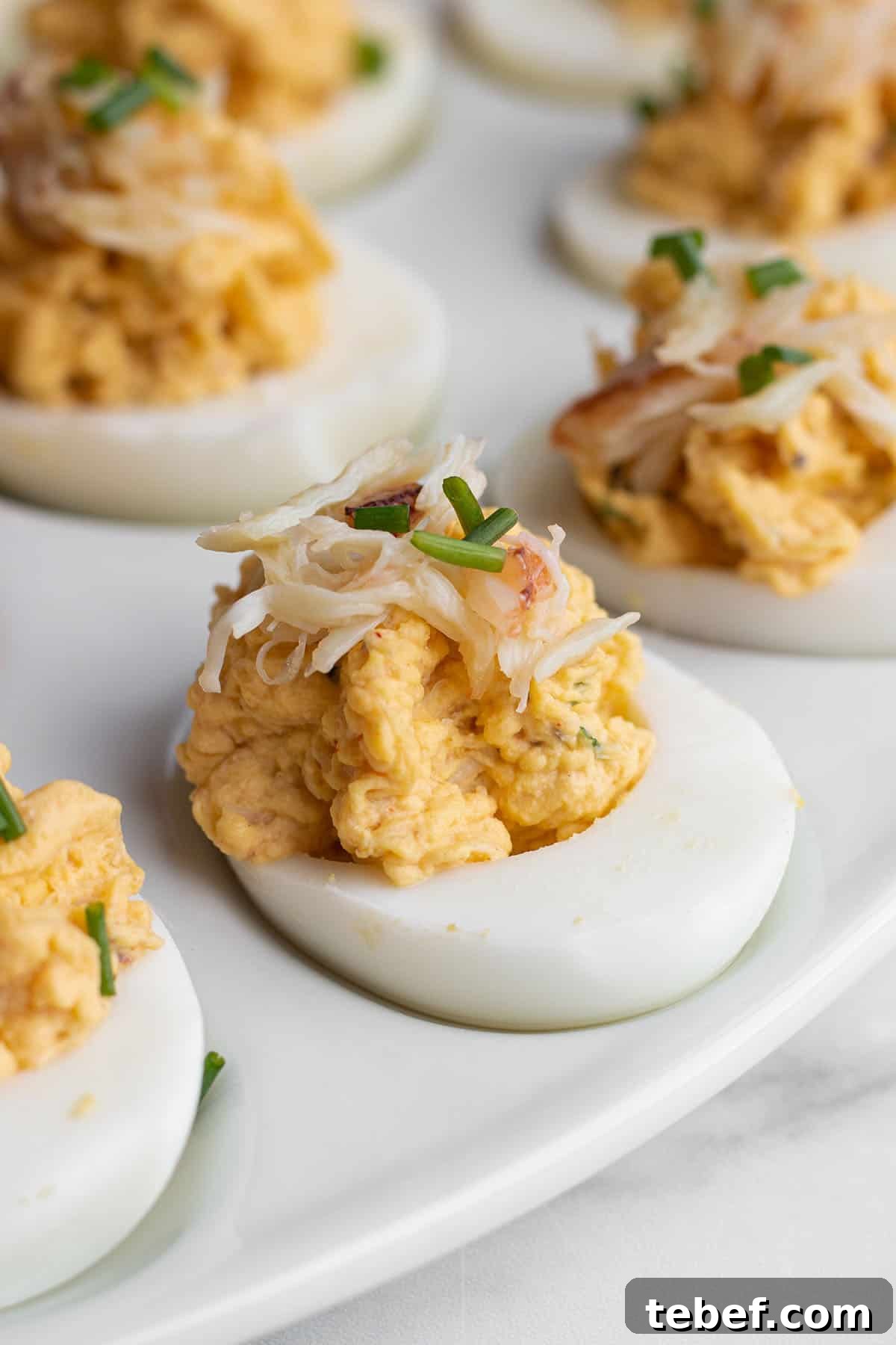A plate with deviled eggs topped with fresh crab and chives. 
