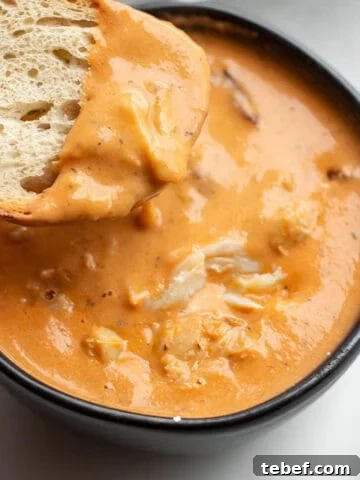 A black bowl with a crab bisque and piece of sourdough being dunked in it.