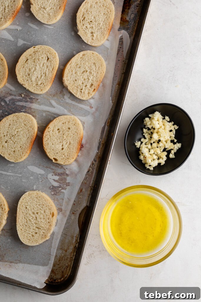 Creamy Sheet-Pan Roasted Tomato Soup Recipe 13 sliced baguette pieces on a parchment lined sheet pan with minced garlic and olive oil