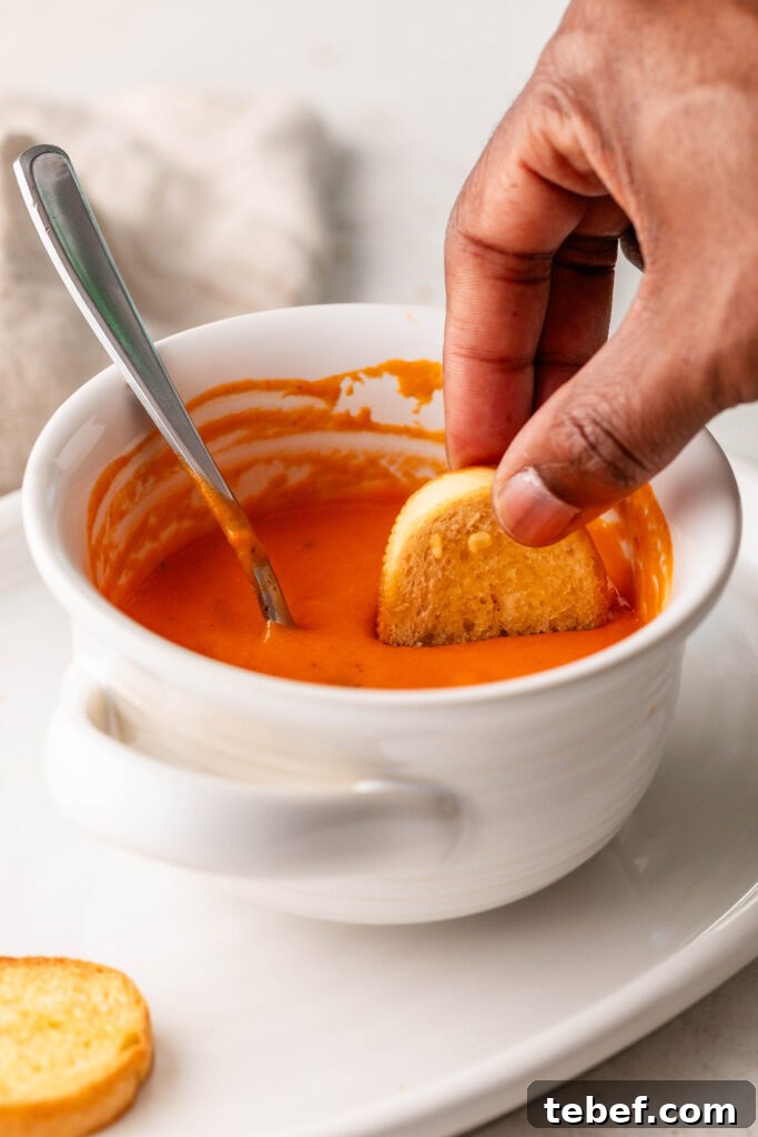 Creamy Sheet-Pan Roasted Tomato Soup Recipe 14 dipping a garlic crostini in a bowl of creamy roasted tomato soup