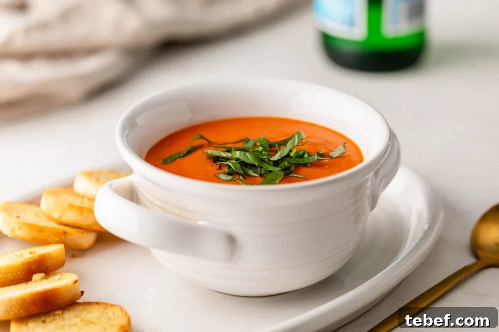 Creamy Sheet-Pan Roasted Tomato Soup Recipe 16 bowl of creamy roasted tomato soup topped with fresh basil on a plate with garlic crostini and a gold spoon