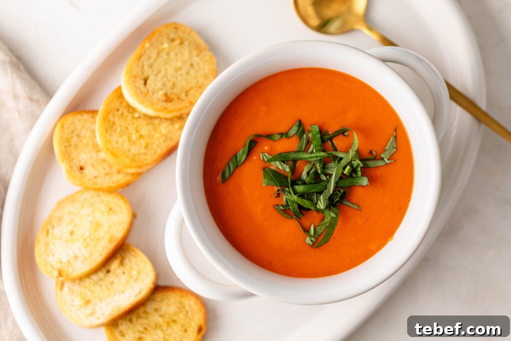 Creamy Sheet-Pan Roasted Tomato Soup Recipe 17 bowl of creamy roasted tomato soup topped with fresh basil on a plate with garlic crostini and a gold spoon