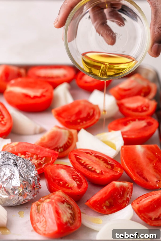 Creamy Sheet-Pan Roasted Tomato Soup Recipe 7 pouring olive oil over tomatoes and onions