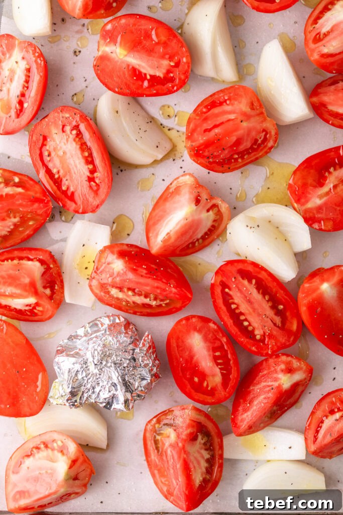 Creamy Sheet-Pan Roasted Tomato Soup Recipe 8 oiled and seasoned tomatoes and onions with wrapped garlic on a parchment lined sheet pan