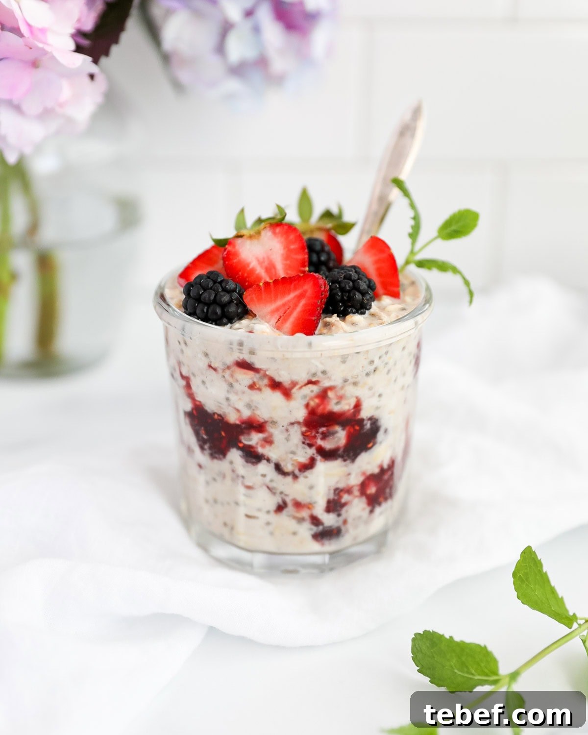 Peanut butter and jelly overnight oats in a jar with fresh fruit and a spoon.