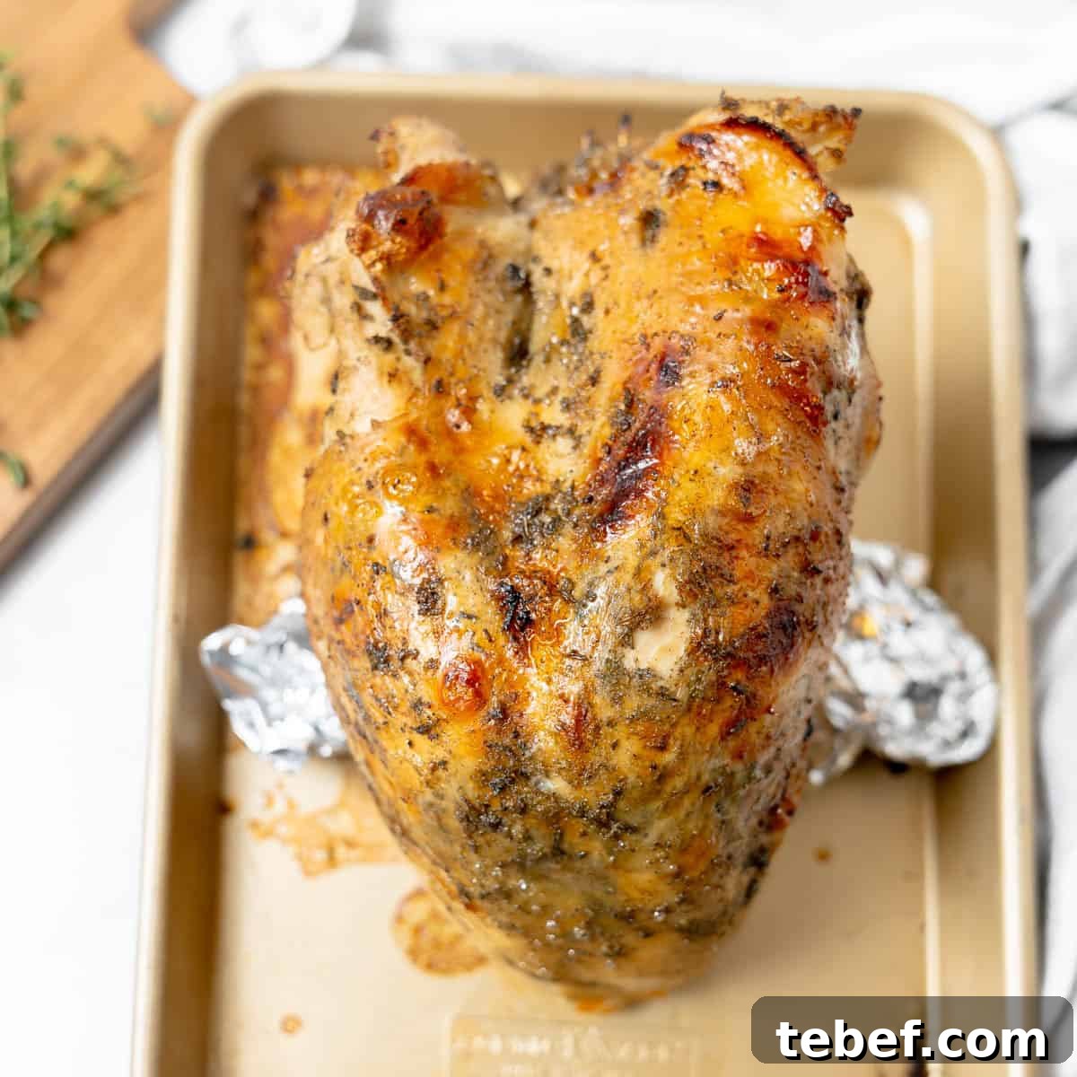 A cooked, seasoned turkey breast sits on a baking tray, with foil-wrapped ends visible underneath.
