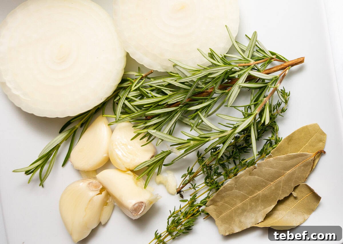 Sliced onion, garlic cloves, fresh rosemary and thyme sprigs, and two dried bay leaves arranged on a white surface.