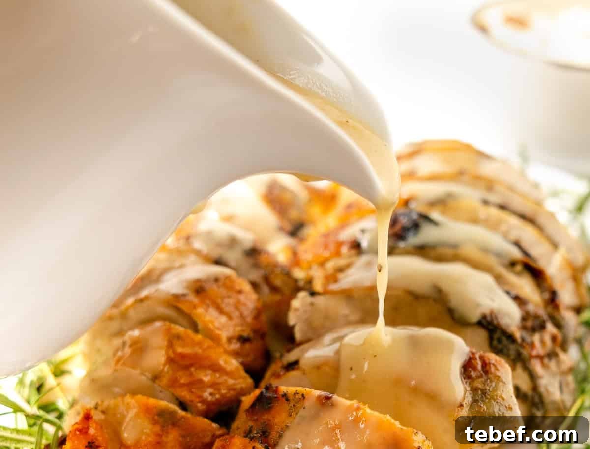 Sliced roasted meat is topped with creamy gravy being poured from a white sauce boat.