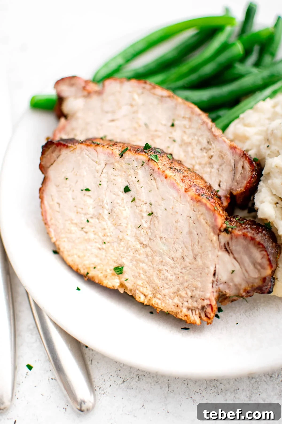 Perfect Oven-Roasted Pork Loin: Juicy, Crispy Recipe and Tips 2 A detailed close-up of two thick slices of pork loin, showing the juicy interior and seasoned crust. The slices rest beside smooth mashed potatoes and vibrant green beans, all on a white plate.