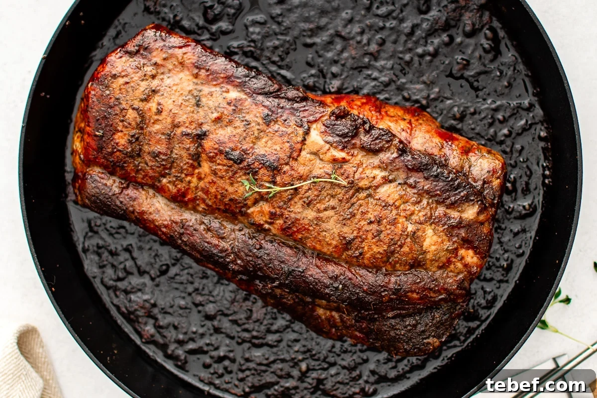 Perfect Oven-Roasted Pork Loin: Juicy, Crispy Recipe and Tips 6 A golden-brown, oven-roasted pork loin sits in a large cast iron skillet. The roast is seared and glistening, indicating it's just come out of the oven and is ready to rest before slicing.