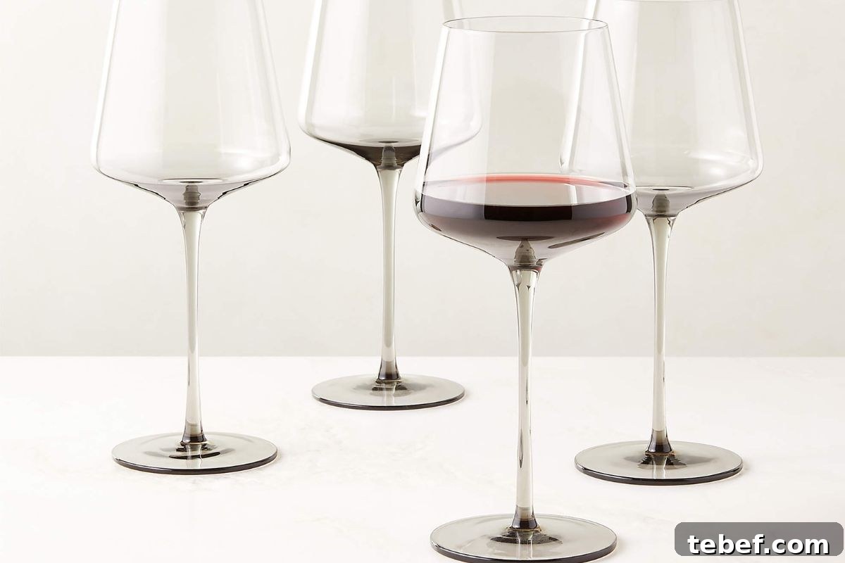 Four empty wine glasses and one partially filled with red wine are arranged on a white surface.