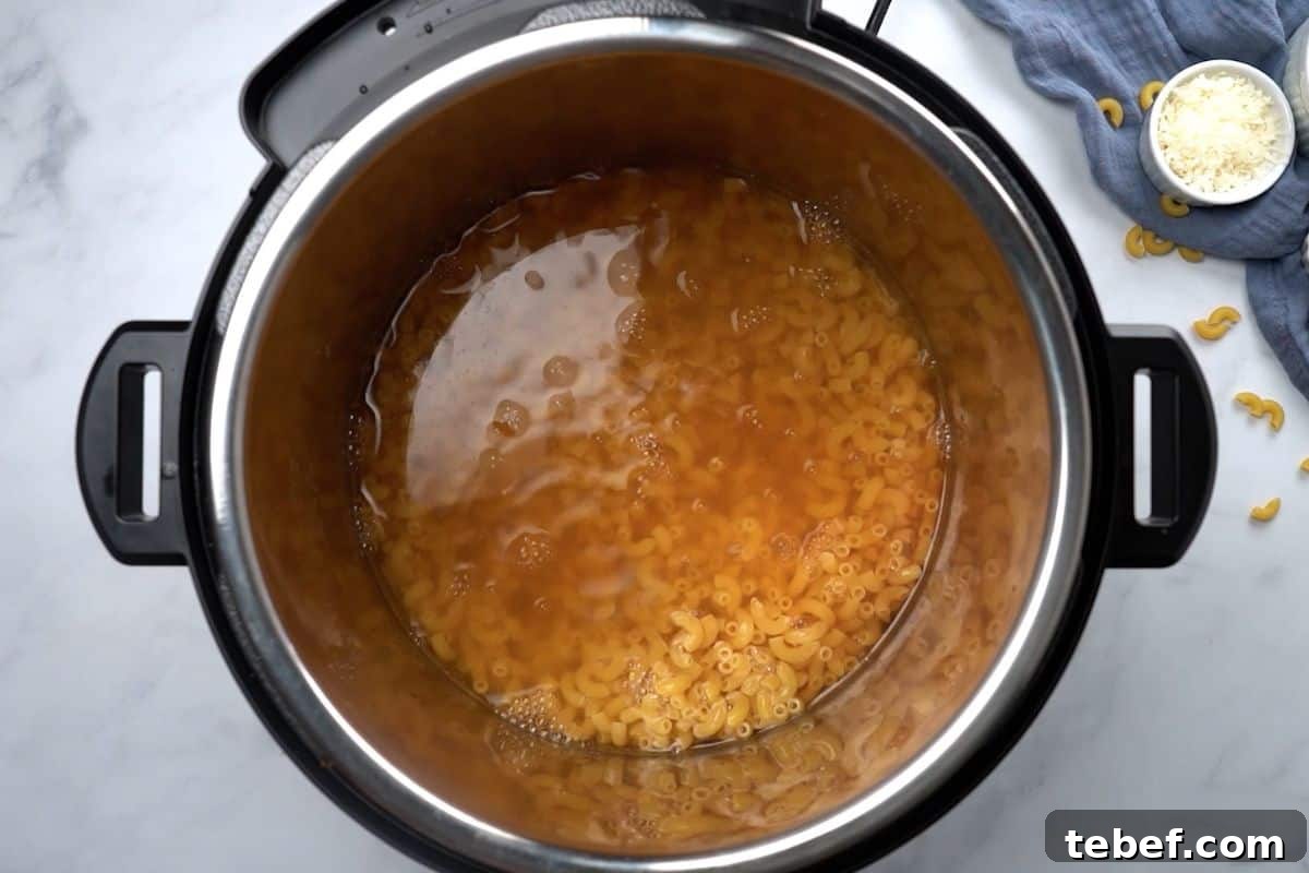 Elbow noodles submerged in seasoned broth insider inner pot for mac and cheese recipe.