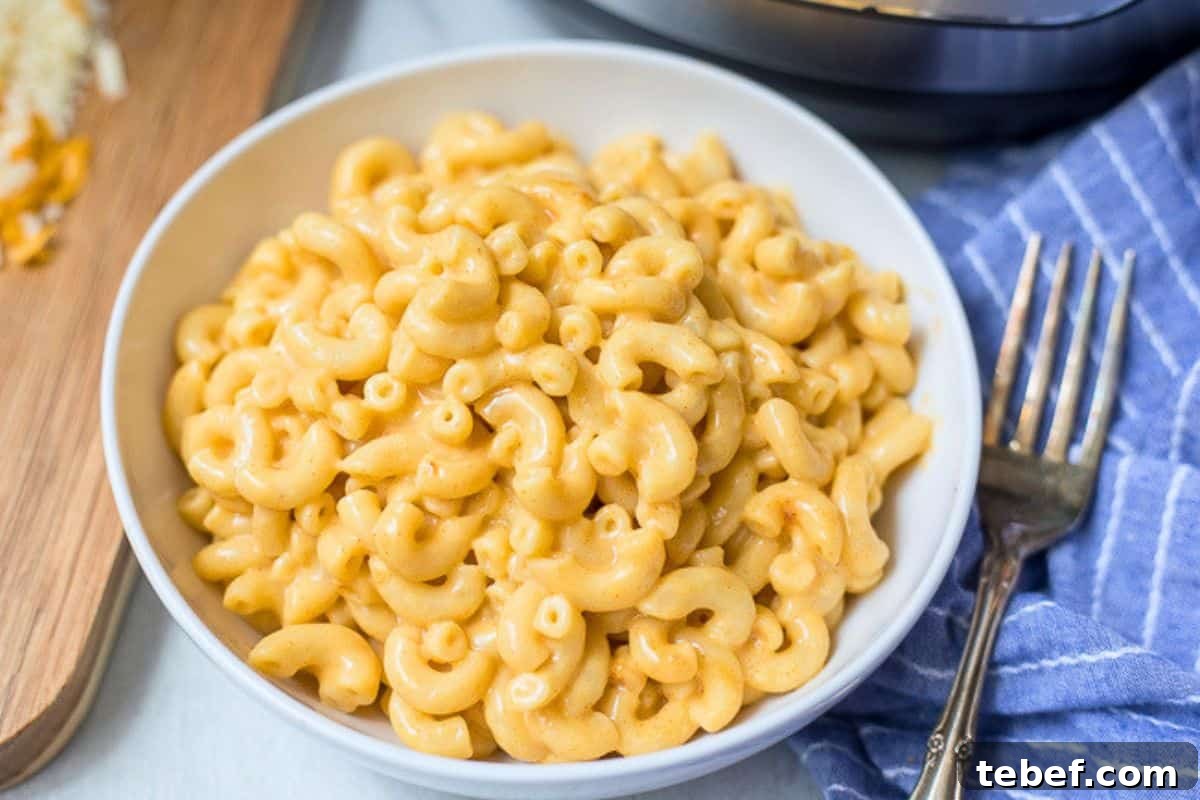 Bowl of creamy mac and cheese served in white dish with shredded cheese off to side.
