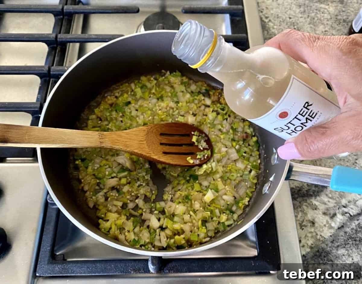 I am adding white wine to the leek and onion mixture in a pan on the stove.