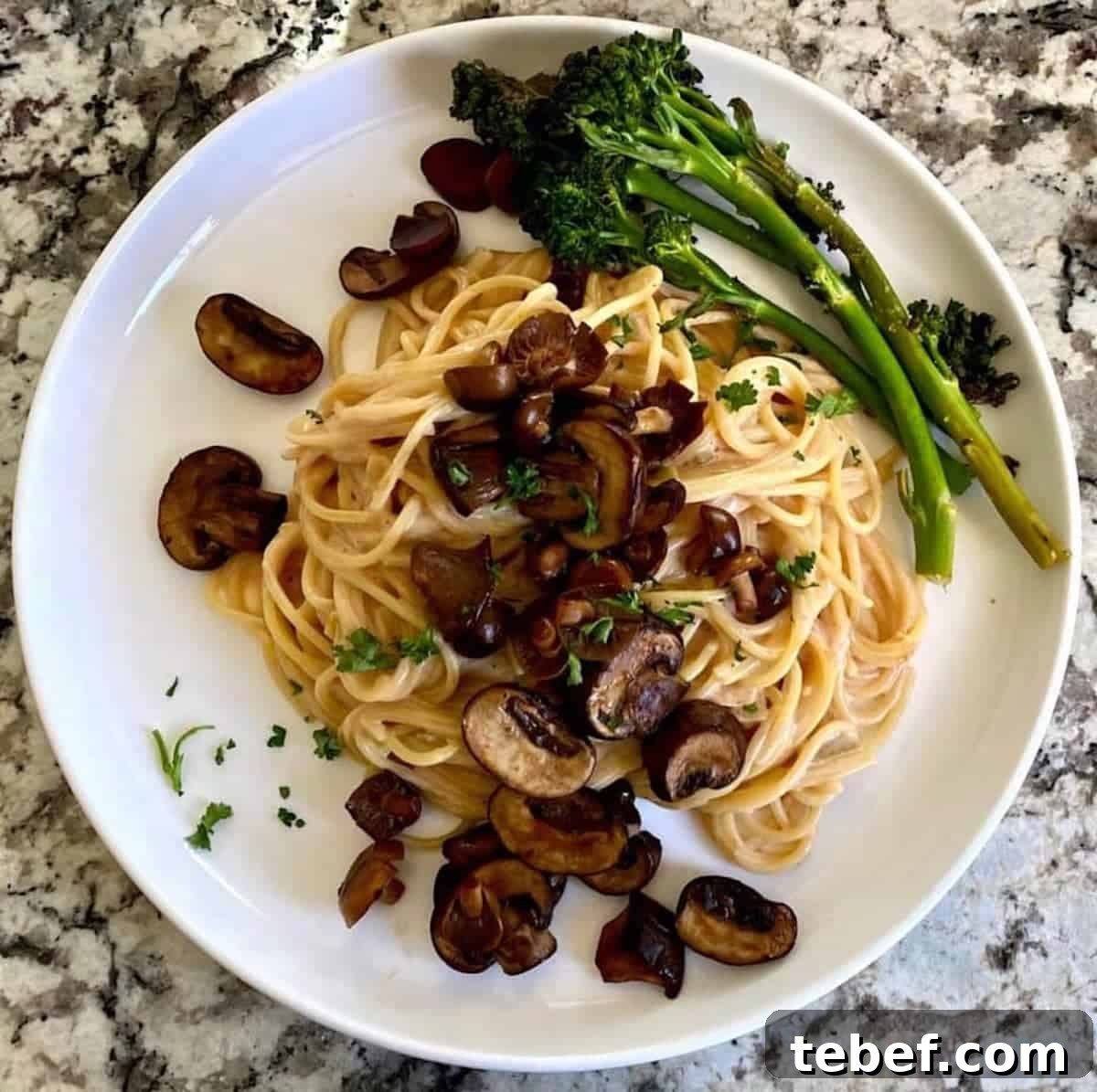 Creamy mushroom pasta recipe on a plate served with broccolini and garnished with parsley on the table.