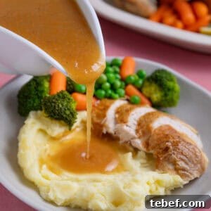 A jug of gluten free gravy being poured over roast chicken and mashed potatoes.