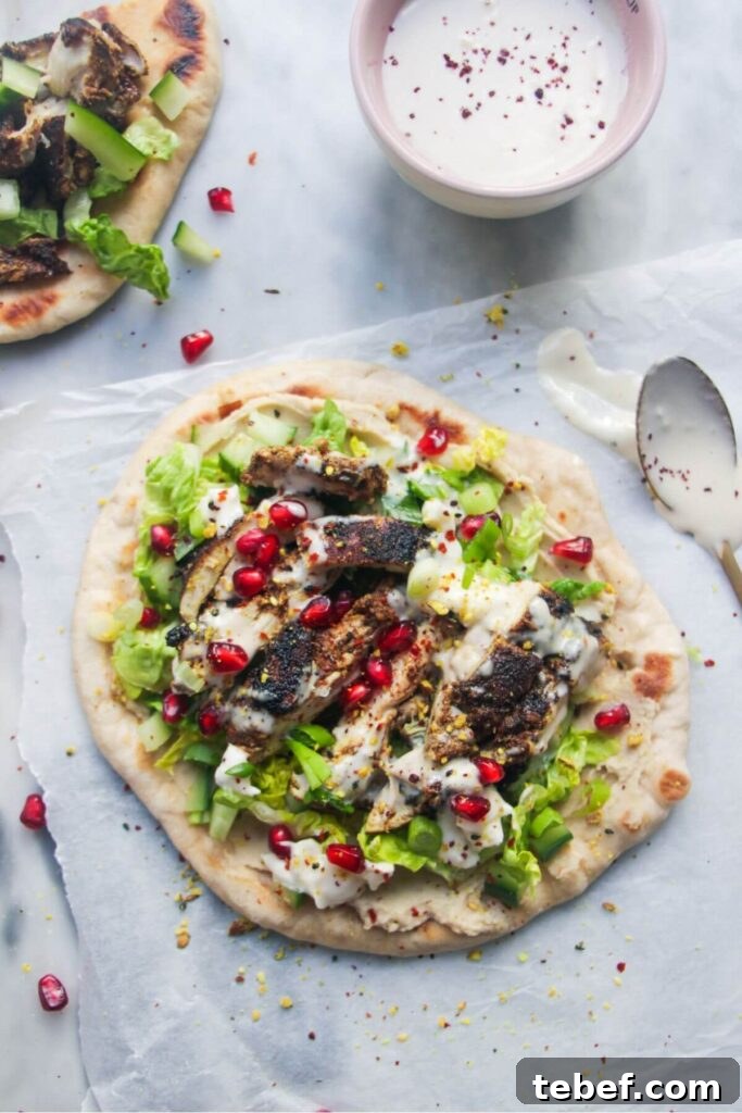 Chicken shawarma wrap on a grey marble background with a small bowl of tahini sauce on the side.