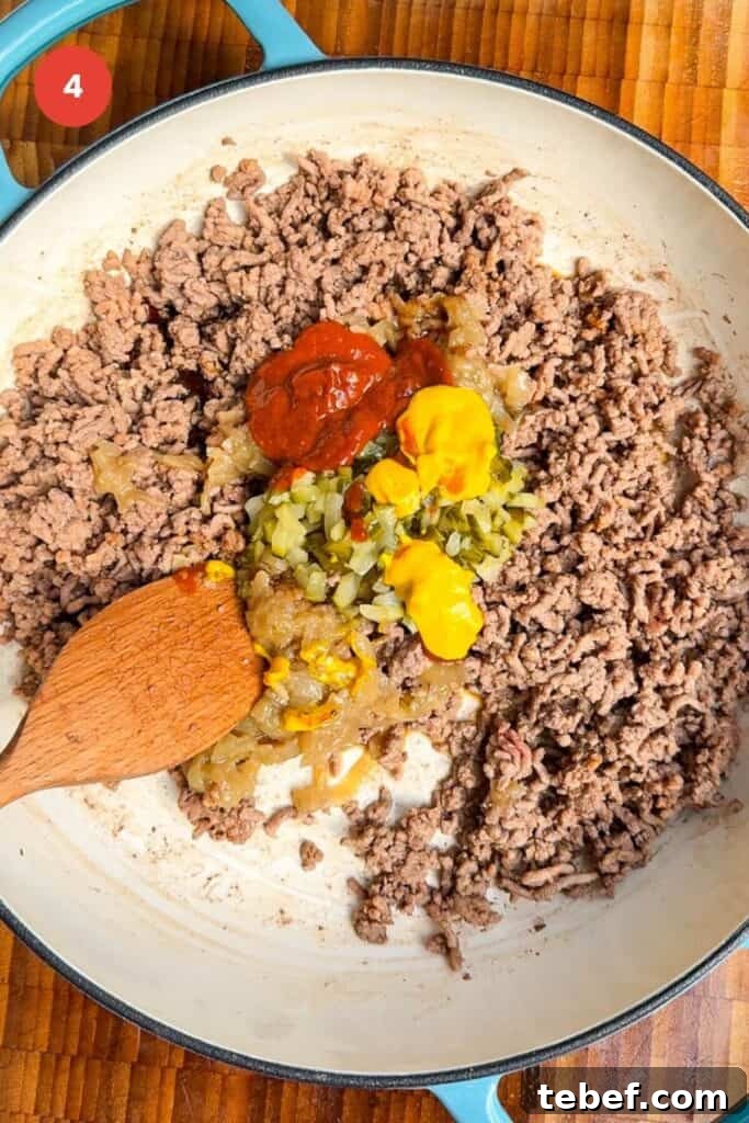 Ground beef browned in a pan, with ketchup, mustard and pickles.