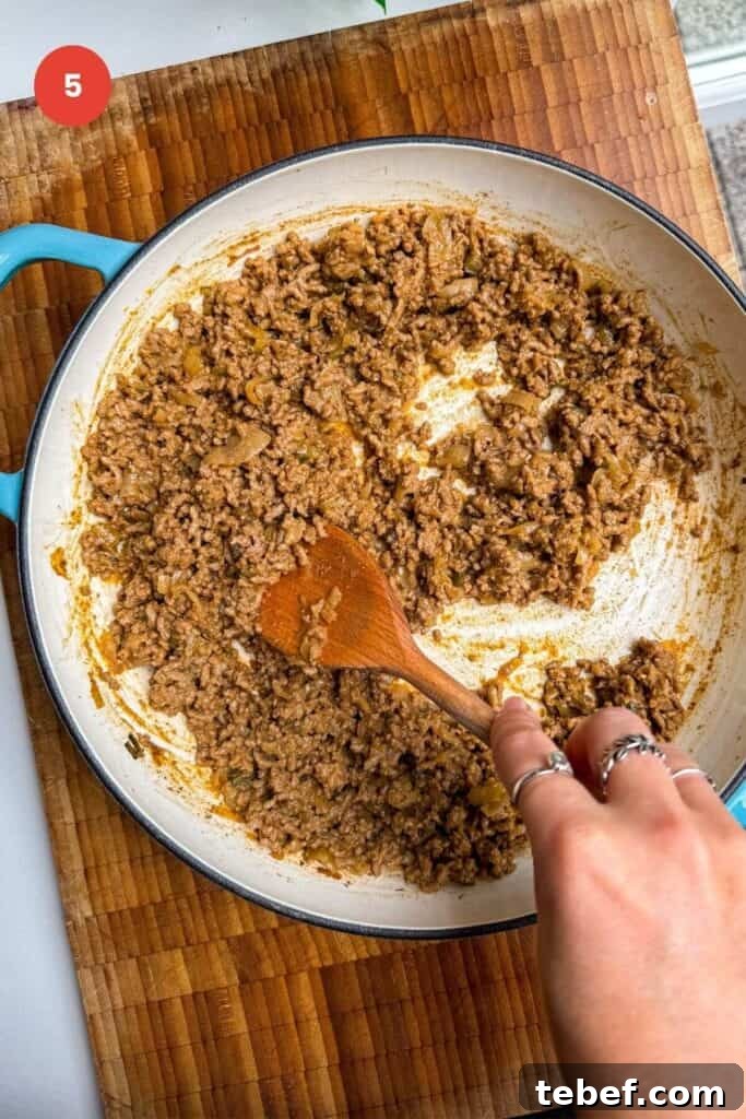 Stirring cheeseburger beef topping in a pan.