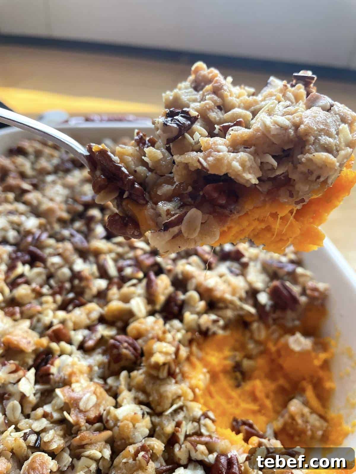 A pan of sweet potato casserole with praline topping with a scoop held above it.