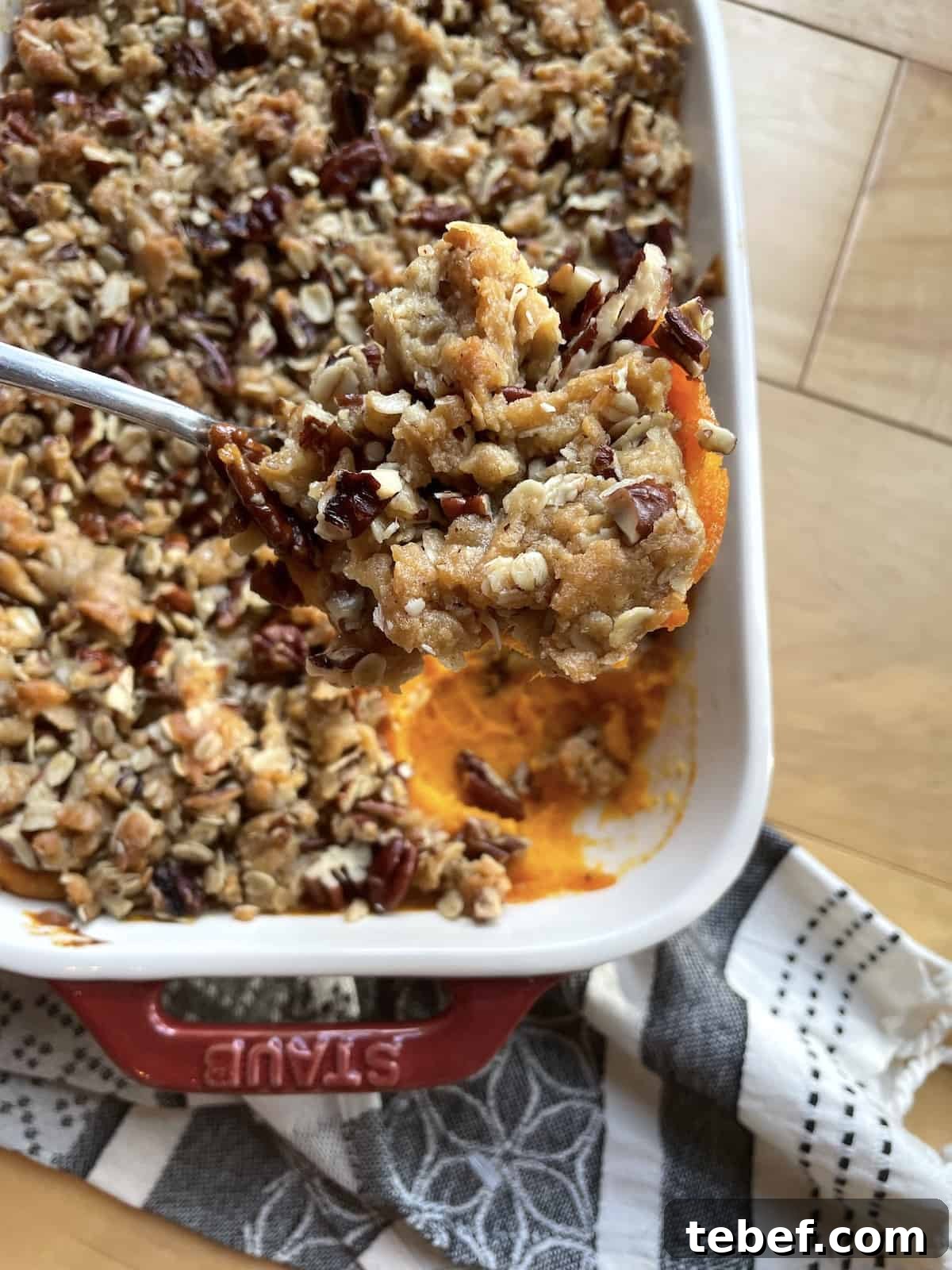 A pan of sweet potato casserole with praline topping with a scoop held above it.