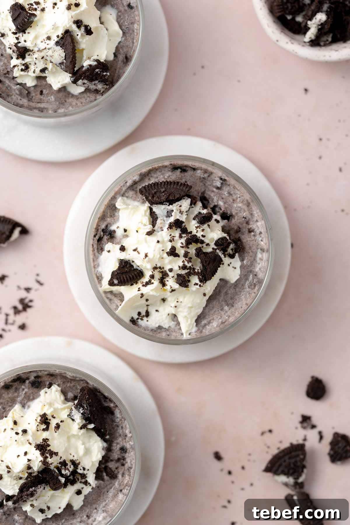 Overhead view of no-bake Oreo cheesecake cups topped with whipped cream and crumbled Oreo cookies.
